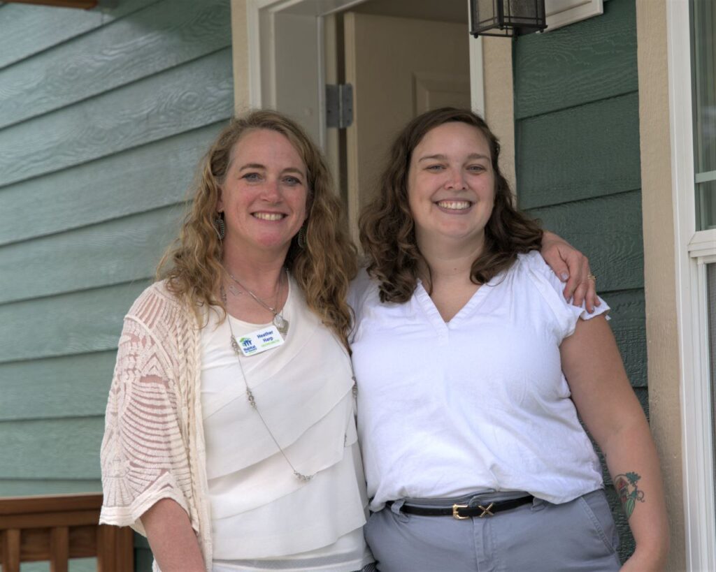 An image of two women smiling in front of a house built by Habitat for Humanity of Missoula.
